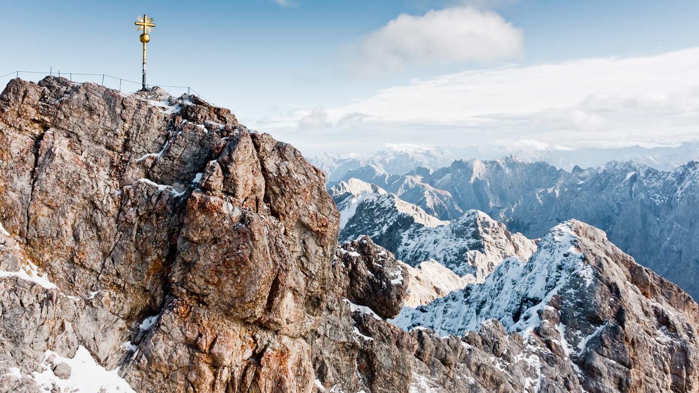 Der höchste Berg Deutschlands, die Zugspitze, mit goldenem Gipfelkreuz und schneebedeckten Gipfeln bei Sonnenschein | © Gettyimages.com/Alexander Reshnya