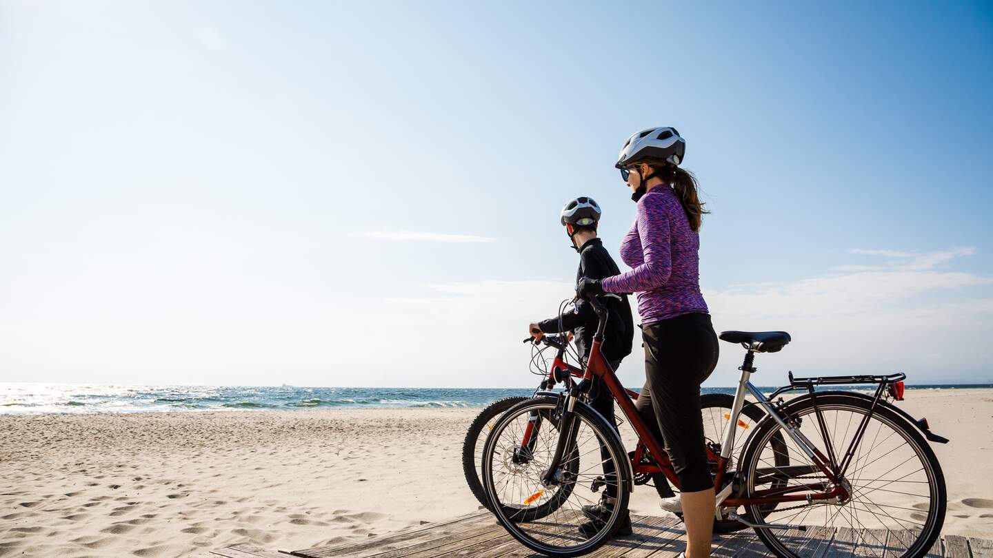 Paar mit Fahrrädern am Strand mit Blicken auf das Meer mit strahlend blauem Himmel | © Gettyimage/gbh007